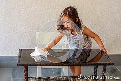Cute child help mom cleaning glass table. Little girl make cleaning in room at home. Stock Photo