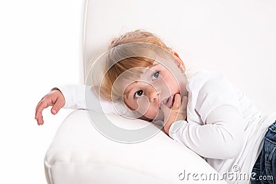 Cute child - shy girl lying on white sofa sucking thumb or finger Stock Photo