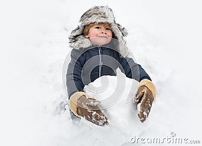 Cute child standing in winter hat with red nose. Joyful kid Having Fun and making snowman in Winter Park. Winter clothes Stock Photo