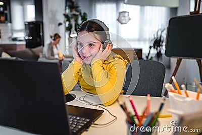 Cute child with headphones using laptop computer for online learning. Home school. Girl doing homework at home Stock Photo