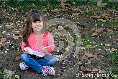 Cute child writing in notebook using pen and smiling. Four years old kid sitting on grass Stock Photo