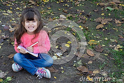 Cute child writing in notebook using pen and smiling. Four years old kid sitting on grass Stock Photo