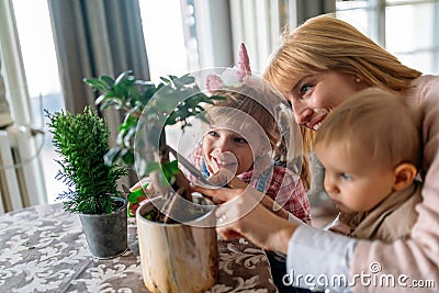 Cute children helping her mother to care for plants. Mom and her kids engaging in gardening at home. Stock Photo
