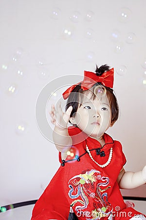 Cute Chinese little baby in red cheongsam play soap bubbles Stock Photo