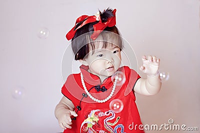 Cute Chinese little baby in red cheongsam play soap bubbles Stock Photo