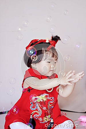 Cute Chinese little baby in red cheongsam play soap bubbles Stock Photo