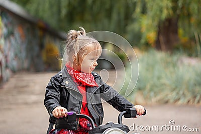 Cute cool child girl in leather jacket riding the motorbike in summer park Stock Photo