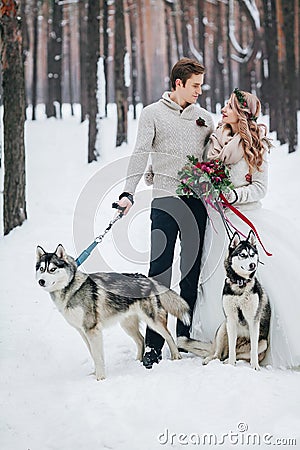 Cute couple with two siberian husky are posed on background of snowy forest. Winter wedding. Artwork Stock Photo