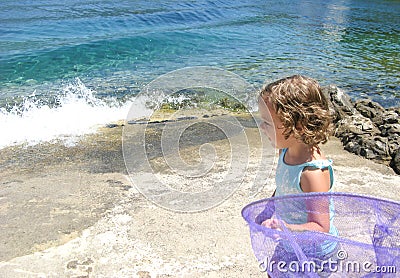 Cute curly blonde toddler girl with butterfly net for catching fish running on the seashore Stock Photo