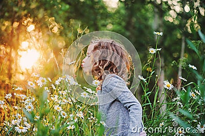 Cute curly child girl smells flower on summer field Stock Photo