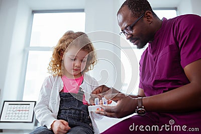 Cute little curly girl taking pills from pleasant pediatrician Stock Photo