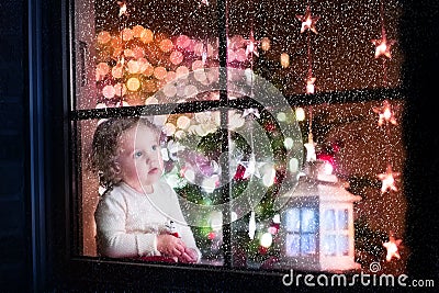 Cute curly toddler girl sitting with a toy bear at home during Christmas time, preparing to celebrate Xmas Eve Stock Photo