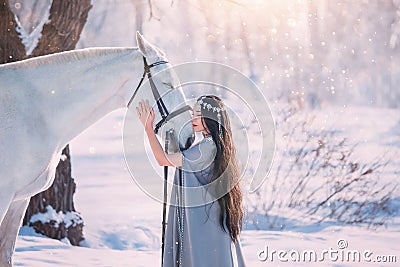 Cute elf princess in long gray cloak and vintage dress, girl with long black wavy curly hair stands next to white Stock Photo