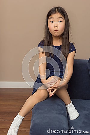 Cute female portrait of little surprised girl, pretty adorable asian relaxed child surprising on blue couch at home Stock Photo