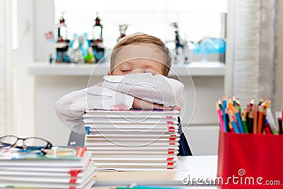 A cute first grader boy in a school uniform at home during a pandemic fell asleep doing homework at a desk with books and pencils Stock Photo