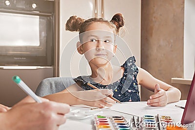 Cute funny caucasian girl with her mother draws with pencils and paints. Online lessons. Quarantined activities for children Stock Photo