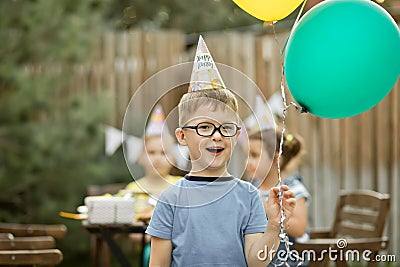 Cute funny four year old boy celebrating his birthday with family or friends in a backyard. Birthday party. Kid wearing party hat Stock Photo