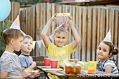 Cute funny nine year old boy celebrating his birthday with family or friends in a backyard. Birthday party. Kid wearing party hat Stock Photo