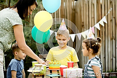 Cute funny nine year old boy celebrating his birthday with family or friends and eating homemade baked cake in a backyard. Stock Photo