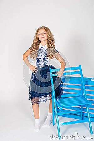 Cute girl with blond curly hair in school fashion clothes with blue chair Stock Photo