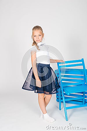 Cute girl with blond curly hair in school fashion clothes with blue chair Stock Photo