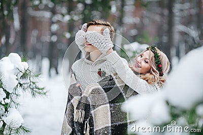 Cute girl covering boyfriend`s eyes by her knitted mittes. Winter wedding. Artwork. Stock Photo