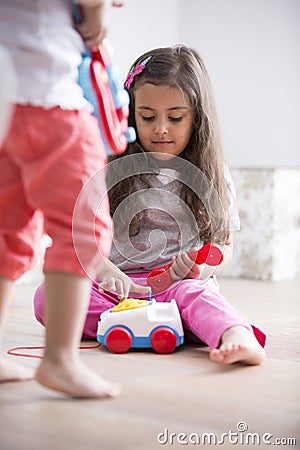 Cute girl dialing the toy telephone while playing with sister at home Stock Photo