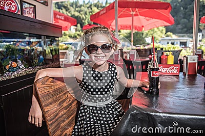 Cute girl drinking a coca cola a 50`s style restaurant with sunglasses Editorial Stock Photo