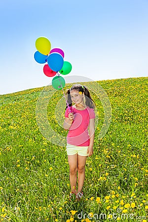 Cute girl with flying balloons stands on grass Stock Photo