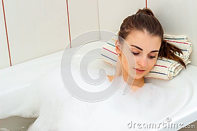 Cute girl with hair collected lies in the bath with foam drooping eyes Stock Photo