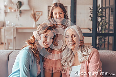 Cute girl, her mother and grandmother smiling at the camera sitting in living room, portrait Stock Photo