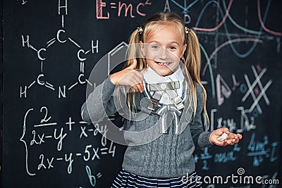 Cute girl in school uniform. Go to school for the first time. Girl indoors of the class room with blackboard on a background shows Stock Photo