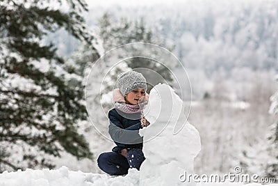 Cute girl sculpts snowman in winter day. Stock Photo