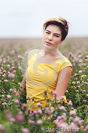 Cute girl with short hair posing sitting in flower field Stock Photo