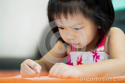 Cute girl studying. Little child uses very short orange crayons to paint in practice book on table. Children do homework. Stock Photo