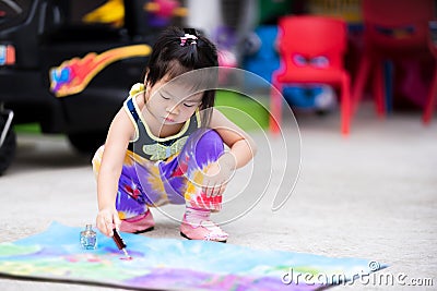 Cute girl is using a nail polish with a glitter to decorate the art on a piece of paper. Asian child intend to make crafts. Stock Photo