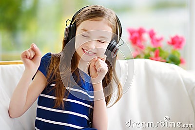 Cute girl wearing huge wireless headphones. Pretty child listening to the music. Schoolgirl having fun listening to kid`s songs at Stock Photo