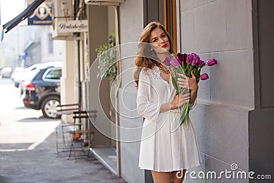 Cute girl in white dress and a beautiful bouquet of tulips. Stock Photo