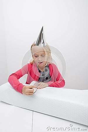 Cute girl wrapping birthday gift at table in house Stock Photo