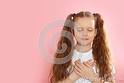 Cute grateful little girl with hands on chest against background. Space for text Stock Photo