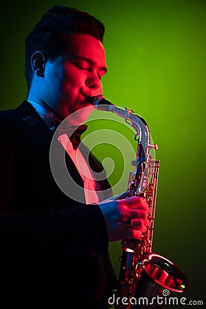 Cute Guy Musician Enjoys Playing the Saxophone, Tenor Saxophone. Neon Light. Close-up Portrait Stock Photo