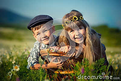 Cute handsome boy wearing jeans and shirt sittingand playing on wooden chair together with beautifull girl on meadow of chamomiles Stock Photo