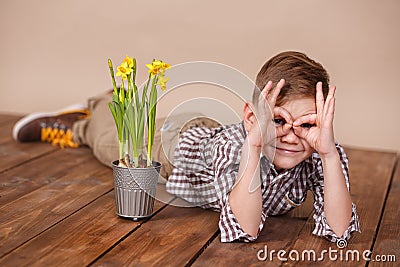 Cute handsome boy on a wooden floor with flowers in basket wearing stylish shirt trousers and boots. Stock Photo