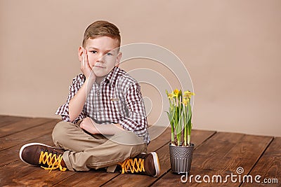 Cute handsome boy on a wooden floor with flowers in basket wearing stylish shirt trousers and boots. Stock Photo