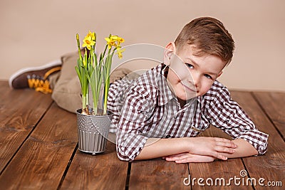 Cute handsome boy on a wooden floor with flowers in basket wearing stylish shirt trousers and boots. Stock Photo