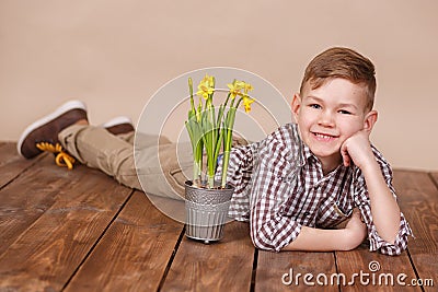 Cute handsome boy on a wooden floor with flowers in basket wearing stylish shirt trousers and boots. Stock Photo