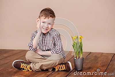 Cute handsome boy on a wooden floor with flowers in basket wearing stylish shirt trousers and boots. Stock Photo