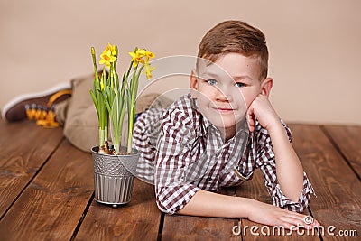 Cute handsome boy on a wooden floor with flowers in basket wearing stylish shirt trousers and boots. Stock Photo