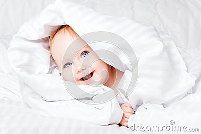 Cute and Happy child with blue eyes looking out of the white blanket. Copy space. Stock Photo