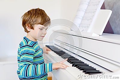 Cute healthy little kid boy playing piano in living room or music school. Preschool child having fun with learning to Stock Photo